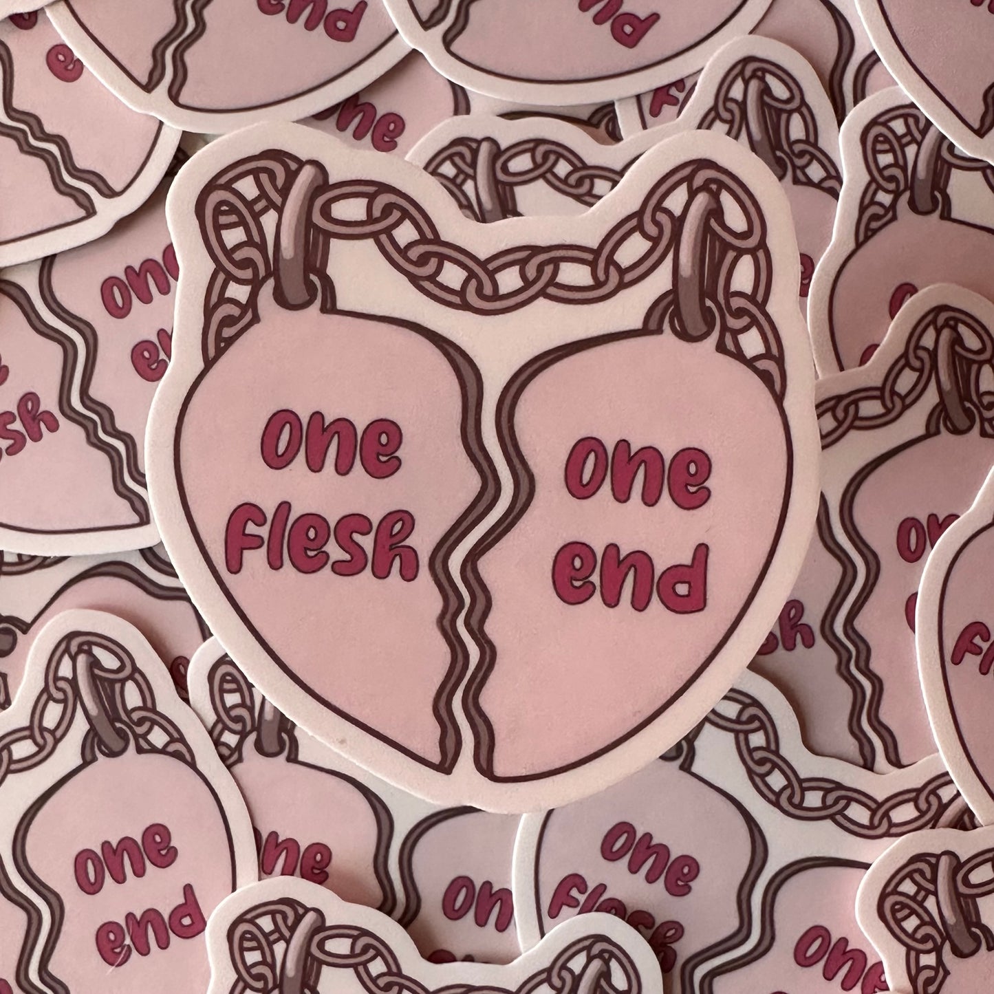 A sticker of a pair of friendship charms in the shape of a broken heart connected by a chain. The left heart has the words "one flesh" on it and the right charm has "one end" on it.