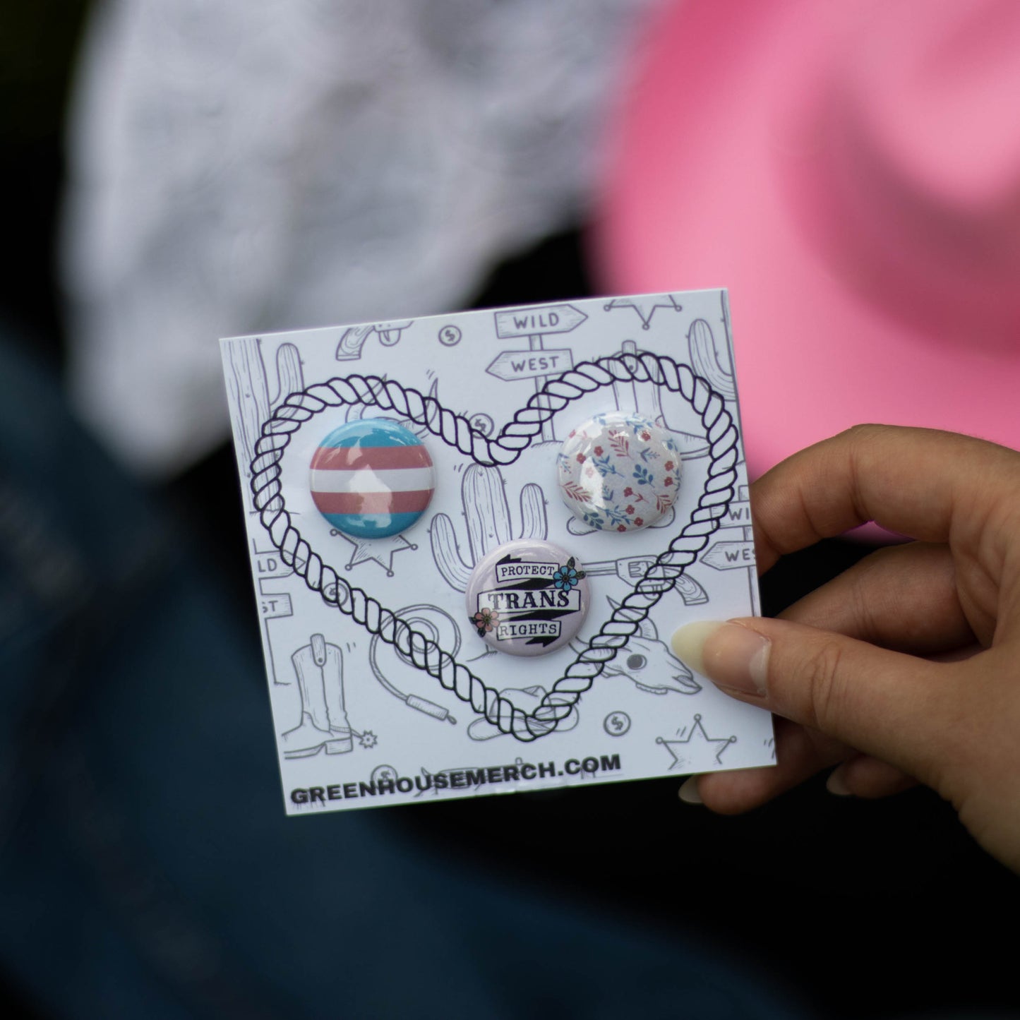 A closeup photo of the Protect Trans Rights button pack. This pack includes 3 one inch trans rights collection buttons: a trans flag button, a "protect trans rights" button, and a subtle floral pattern design featuring colors from the trans flag.