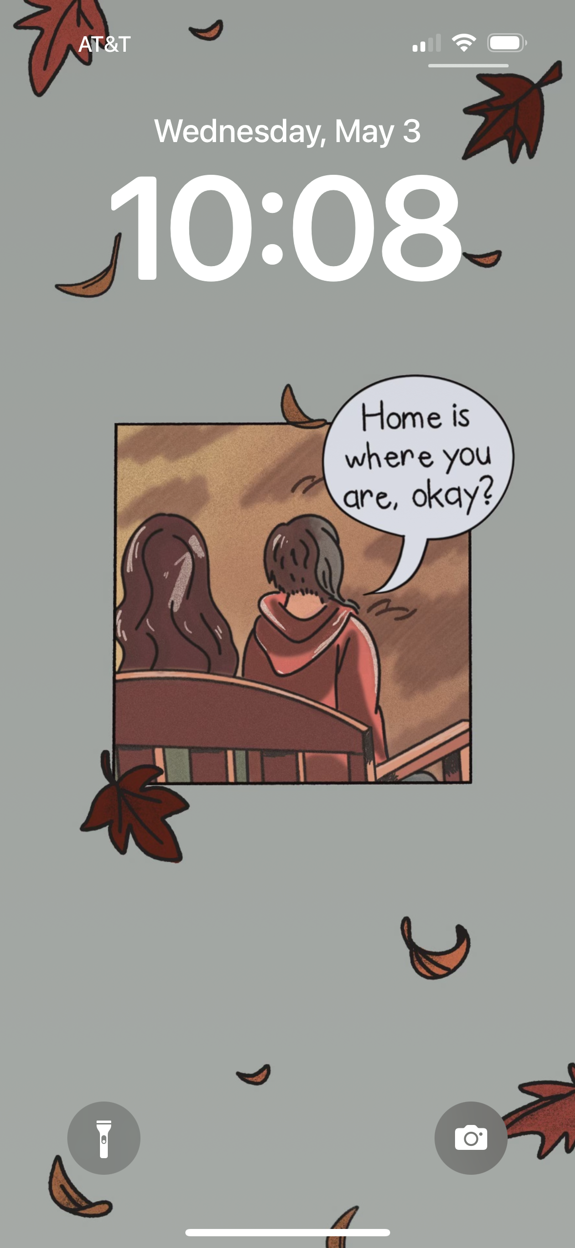 Screenshot of iPhone lockscreen featuring the "home is where you are, okay?" wallpaper. The "home is where you are, okay?" wallpaper features a panel inspired by the graphic novel Mooncakes, where the two main characters are sitting side by side on a bench. Above them is a speech bubble with the phrase "Home is where you are, okay?" written. Additionally, surrounding the panel are various leaves in shades of red and orange.