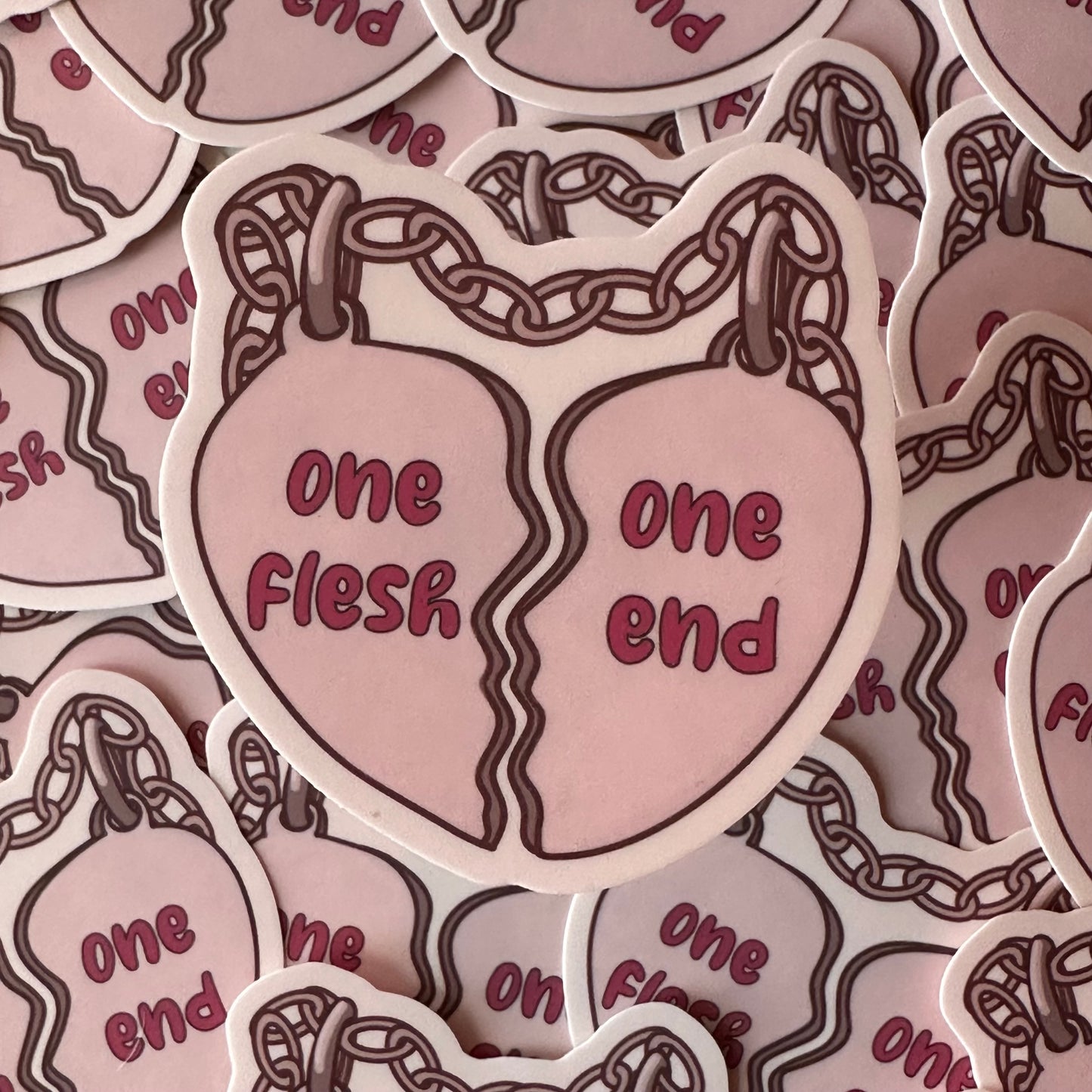 A sticker of a pair of friendship charms in the shape of a broken heart connected by a chain. The left heart has the words "one flesh" on it and the right charm has "one end" on it. 