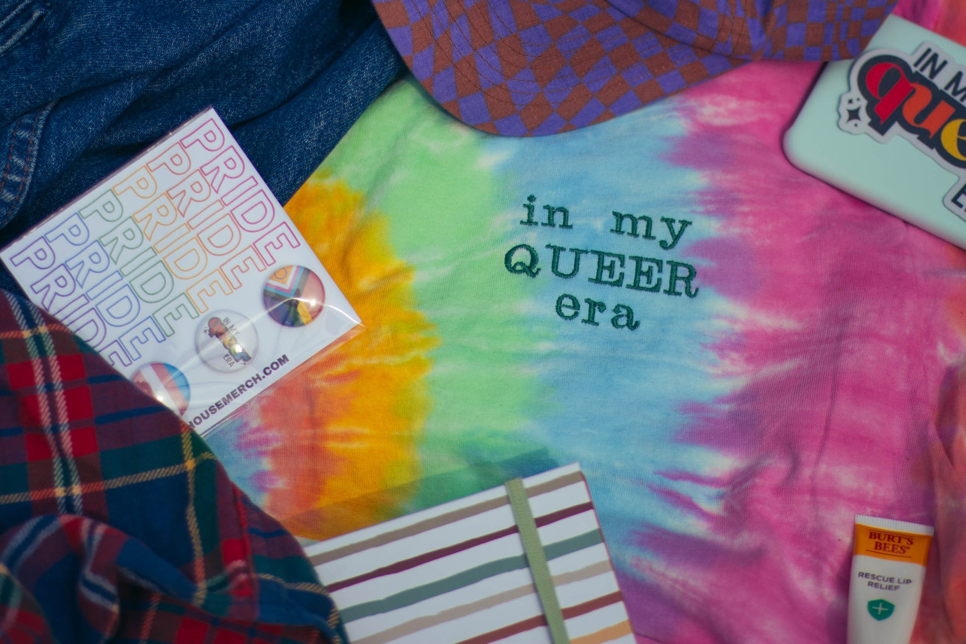 A photo flatlay of various pride designs with the tiedye shirt in the middle.