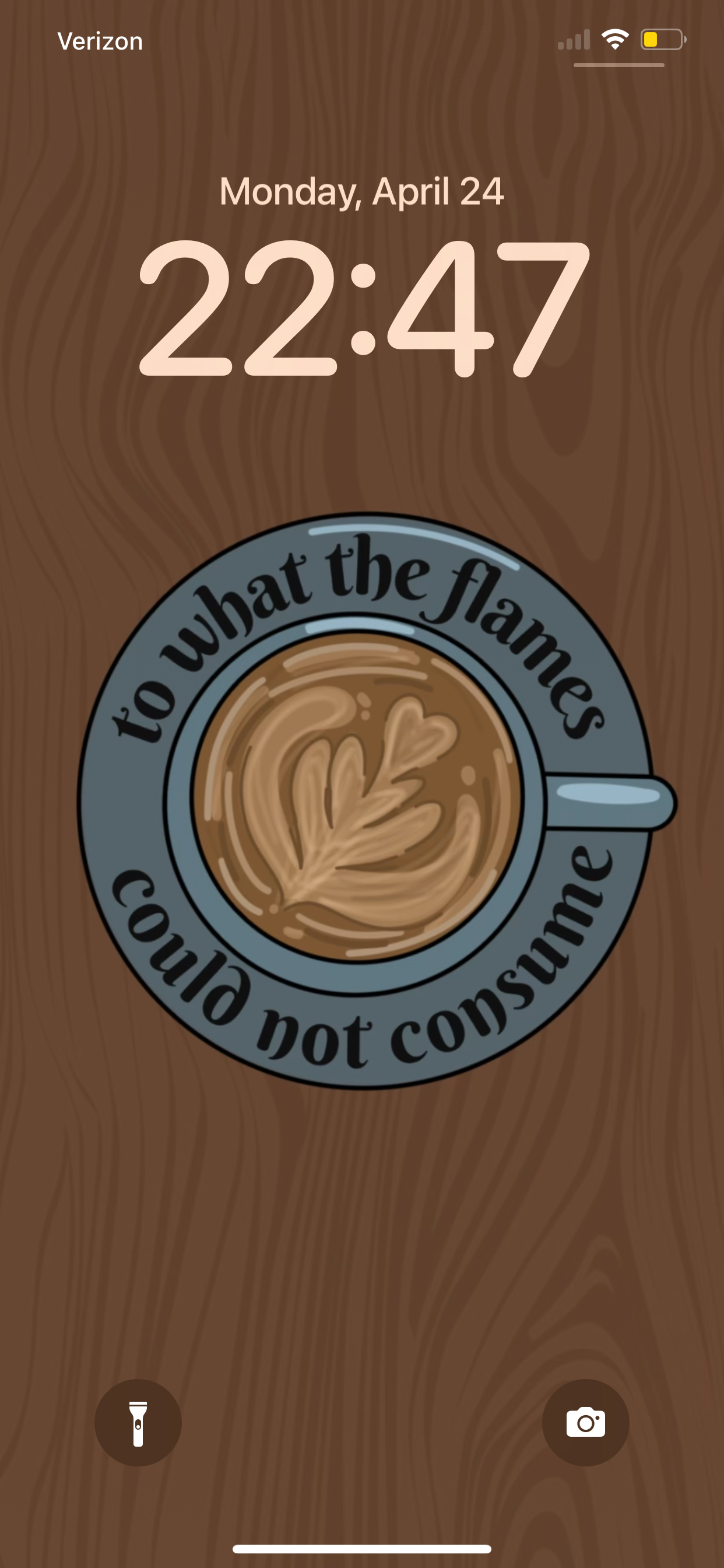 Image of phone lockscreen showing the "to what the flames could not consume" wallpaper. This design features an aerial view of a coffee mug with leafy latte art inside. On the mugs saucer is written the quote: "to what the flames could not consume".