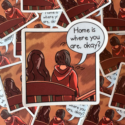 The "home is where you are, okay?" sticker features a panel inspired by the graphic novel Mooncakes, where the two main characters are sitting side by side on a bench. Above them is a speech bubble with the phrase "Home is where you are, okay?" written.