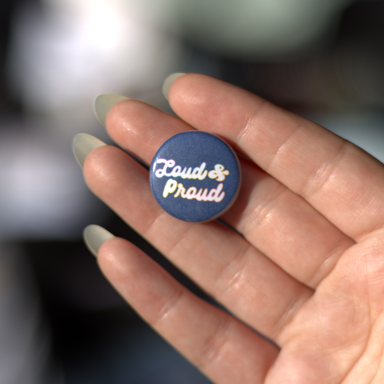 Loud & Proud is on a dark blue background, with the words Loud & Proud written in the center. The letters are in a cursive font and are outlined in a rainbow gradient.