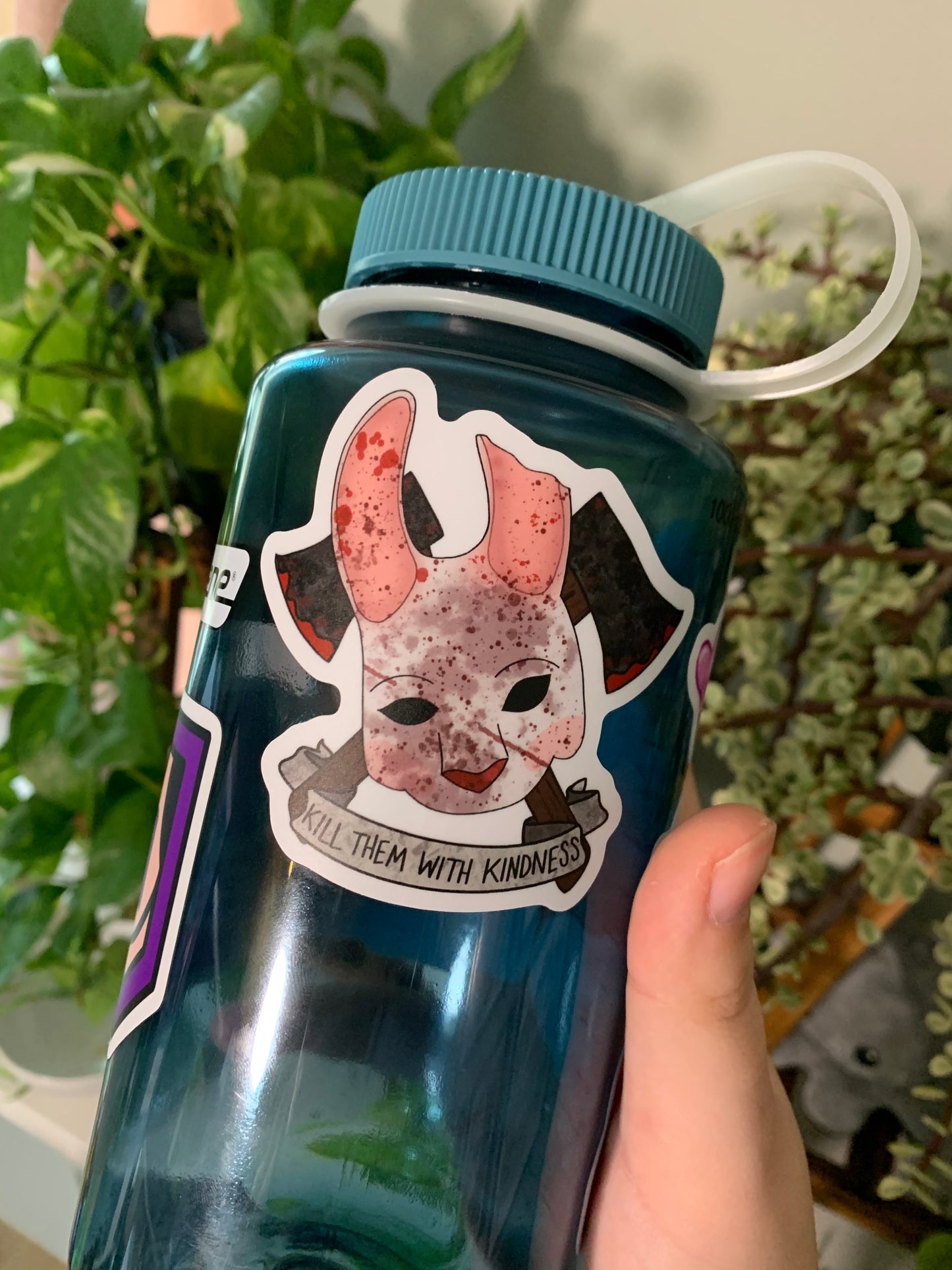 Our Huntress mask sticker featured on a blue nalgene water bottle, held in front of house plants.