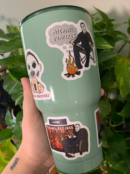 A light green drinking cup with some of the Michael Myers puns stickers on it.